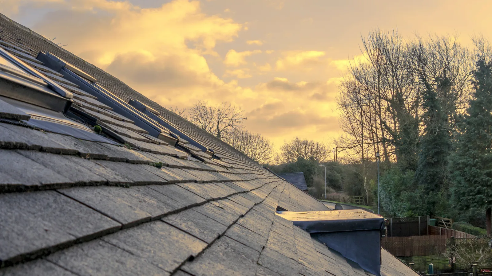 Shingled roof slope and skylights under warm sunset clouds