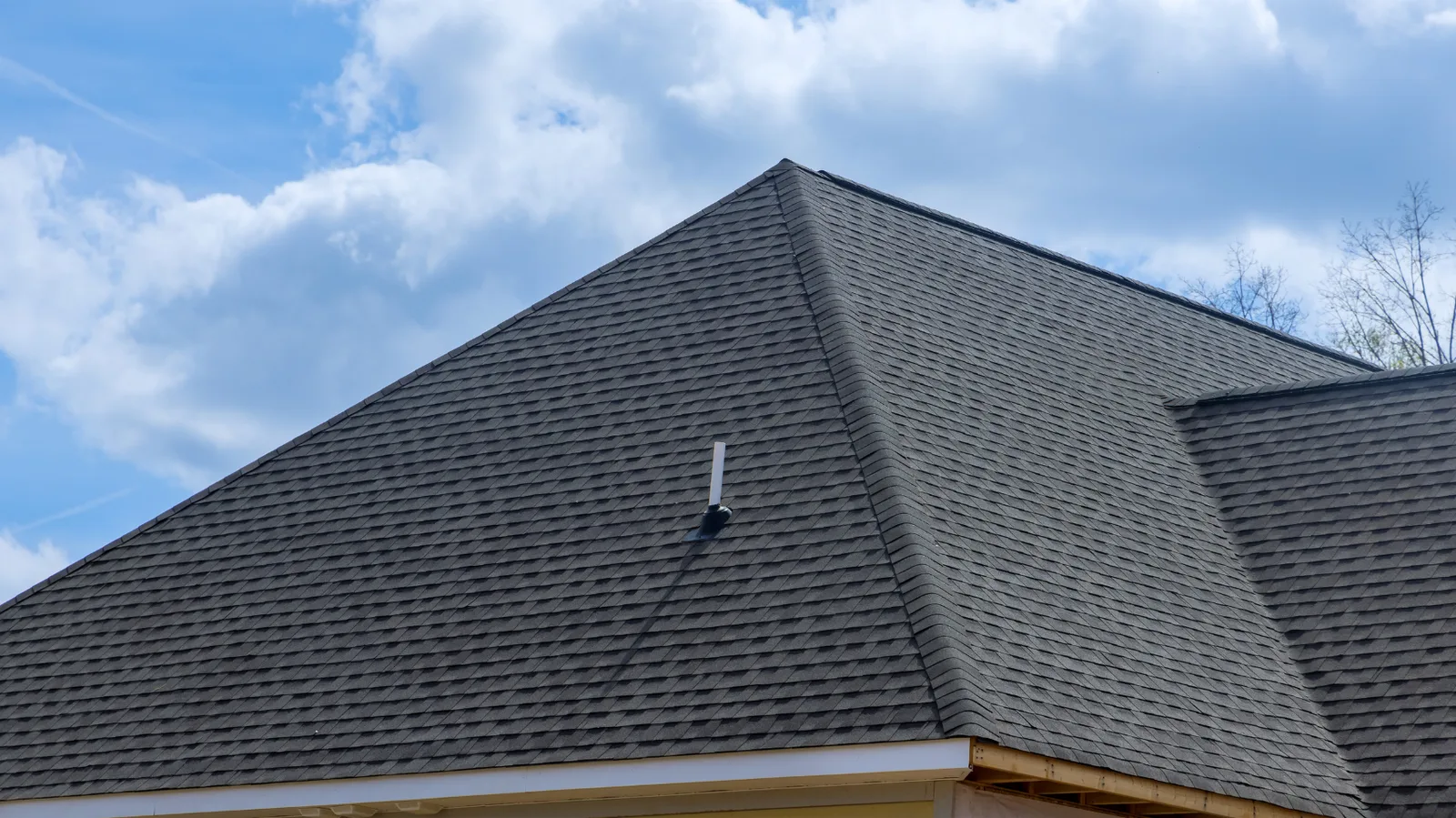 Dark shingle hip roof with a vent pipe under cloudy sky