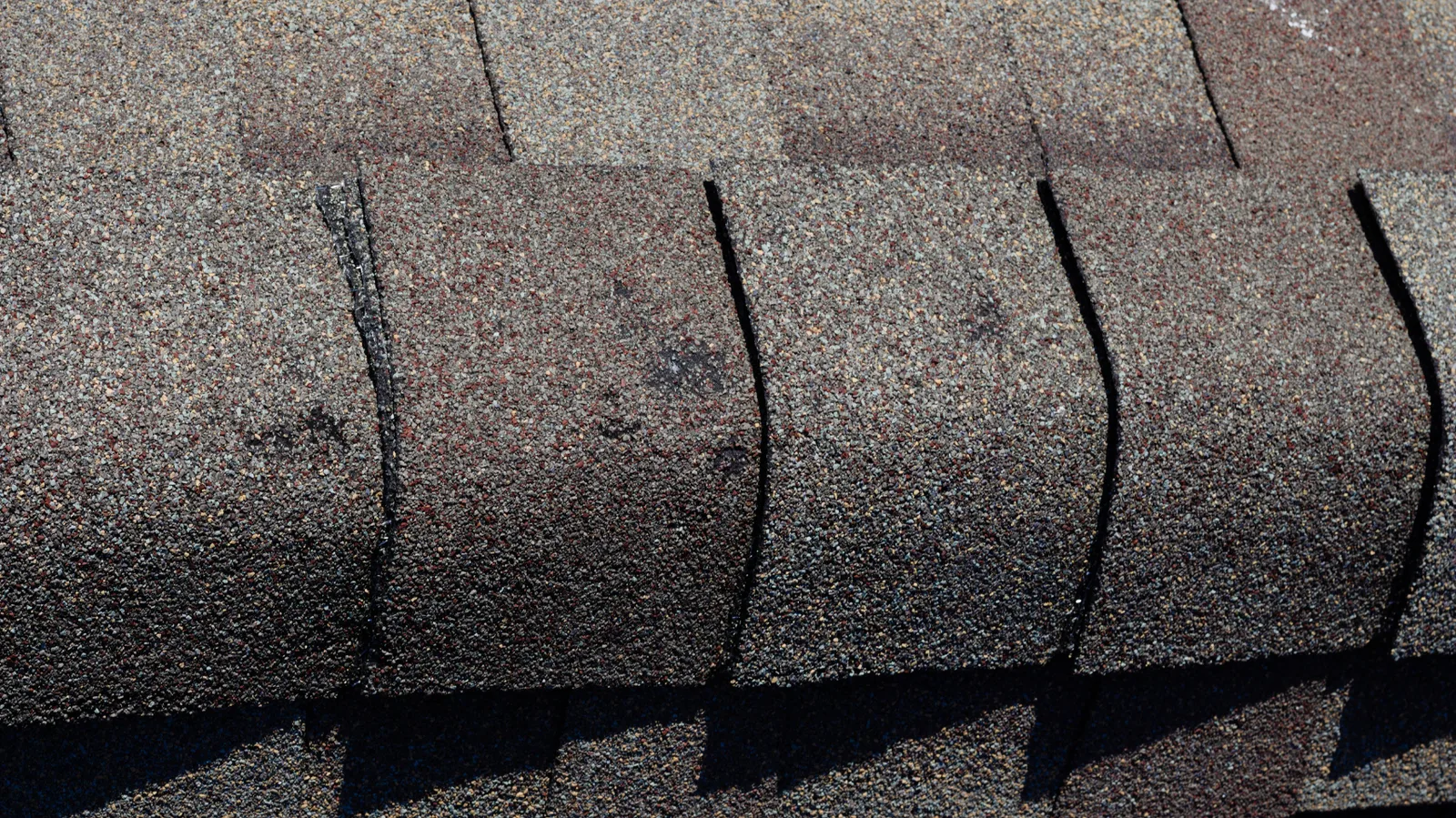 Ridge cap shingles in brown tones on a sunlit asphalt roof
