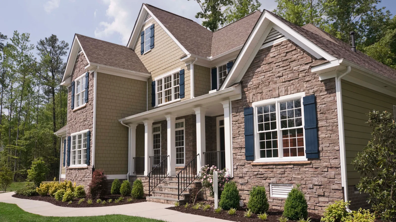 Two-story home with stacked stone and shake siding under a brown shingle roof