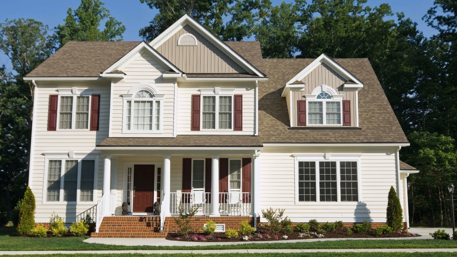 Cream two-story house with brown shingle roof and covered porch