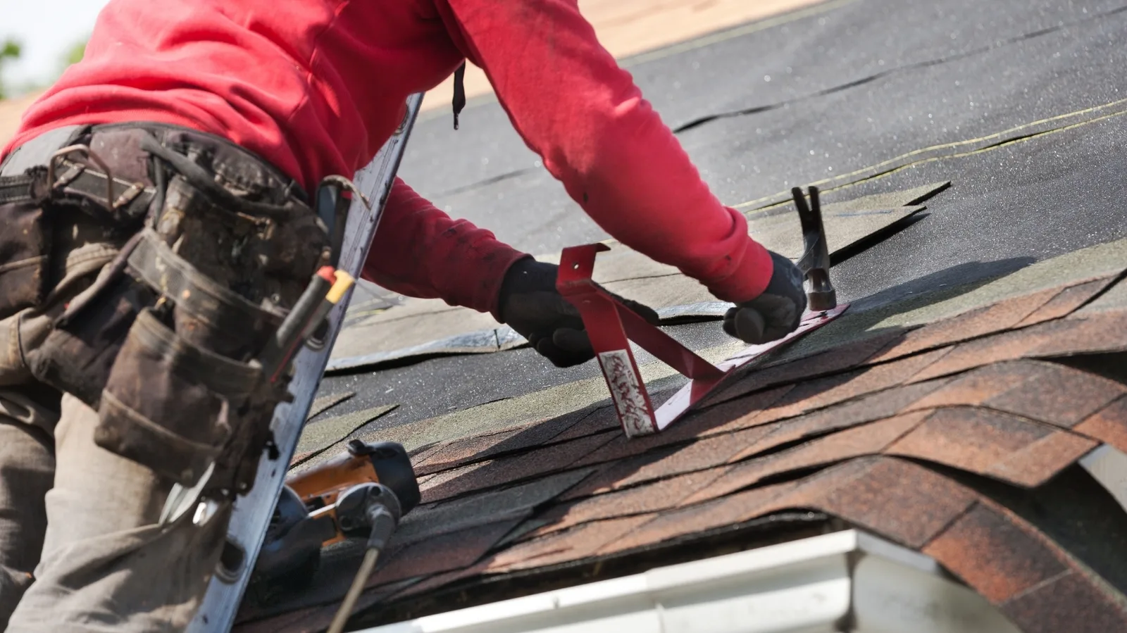 A roofer hammering a roof bracket onto new shingles