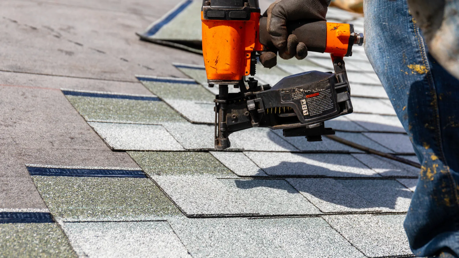 A pneumatic nailer driving nails into new roof shingles