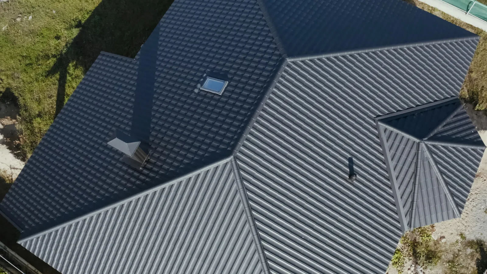 Charcoal metal tile roof slopes meeting above a brick gable and gutter